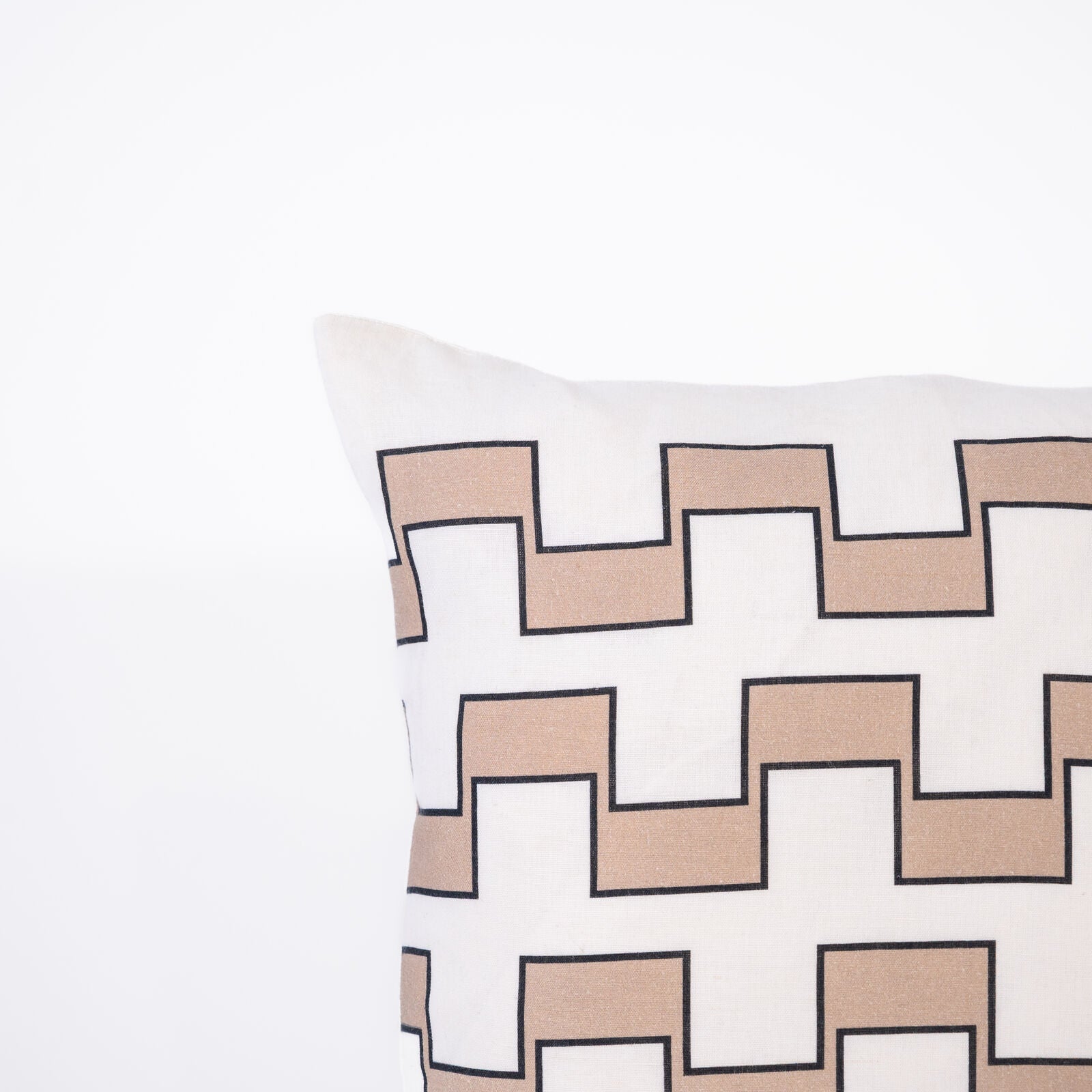 A pillow with a repeating geometric pattern of interlocking beige and white outlined in black on a white background