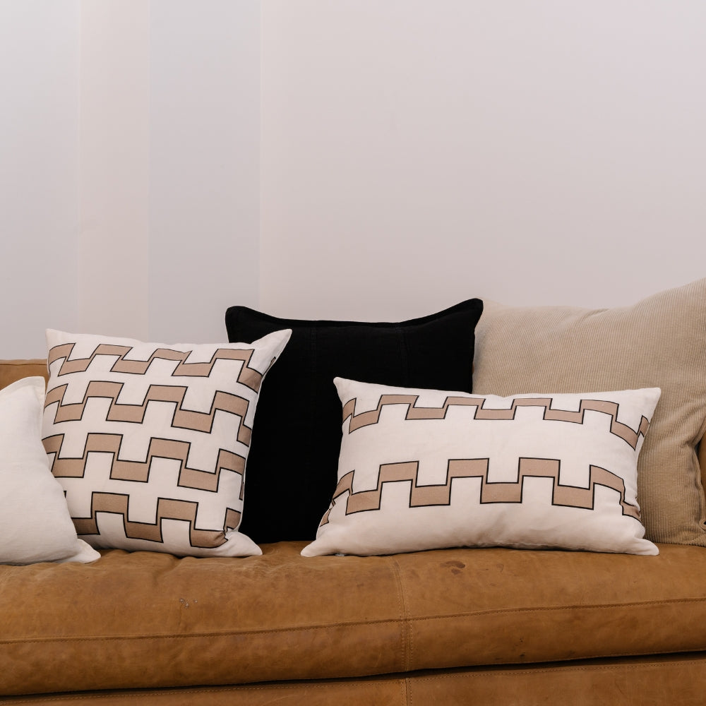 Three decorative pillows on a brown couch against a plain wall.