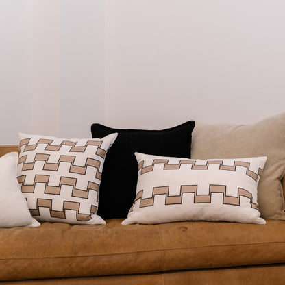 Three decorative pillows on a brown couch against a plain wall.