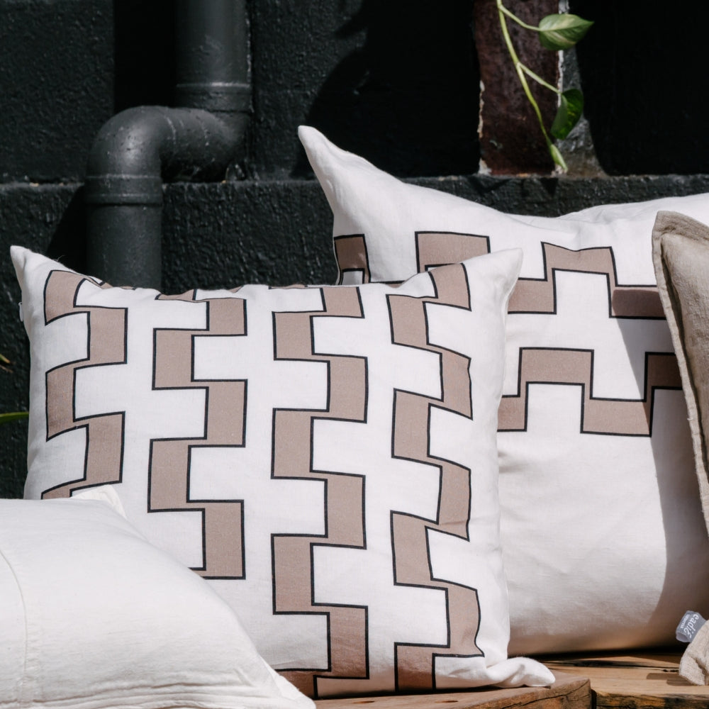 Two pillows with an interlocking beige and white geometric pattern, outlined in black, outdoors.