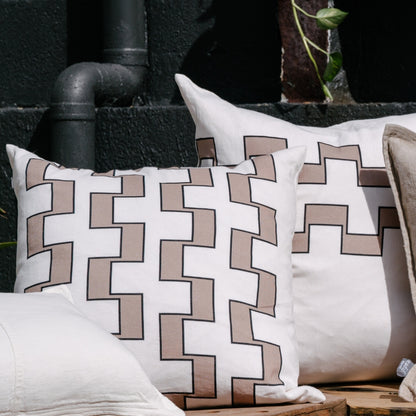 Two pillows with an interlocking beige and white geometric pattern, outlined in black, outdoors.