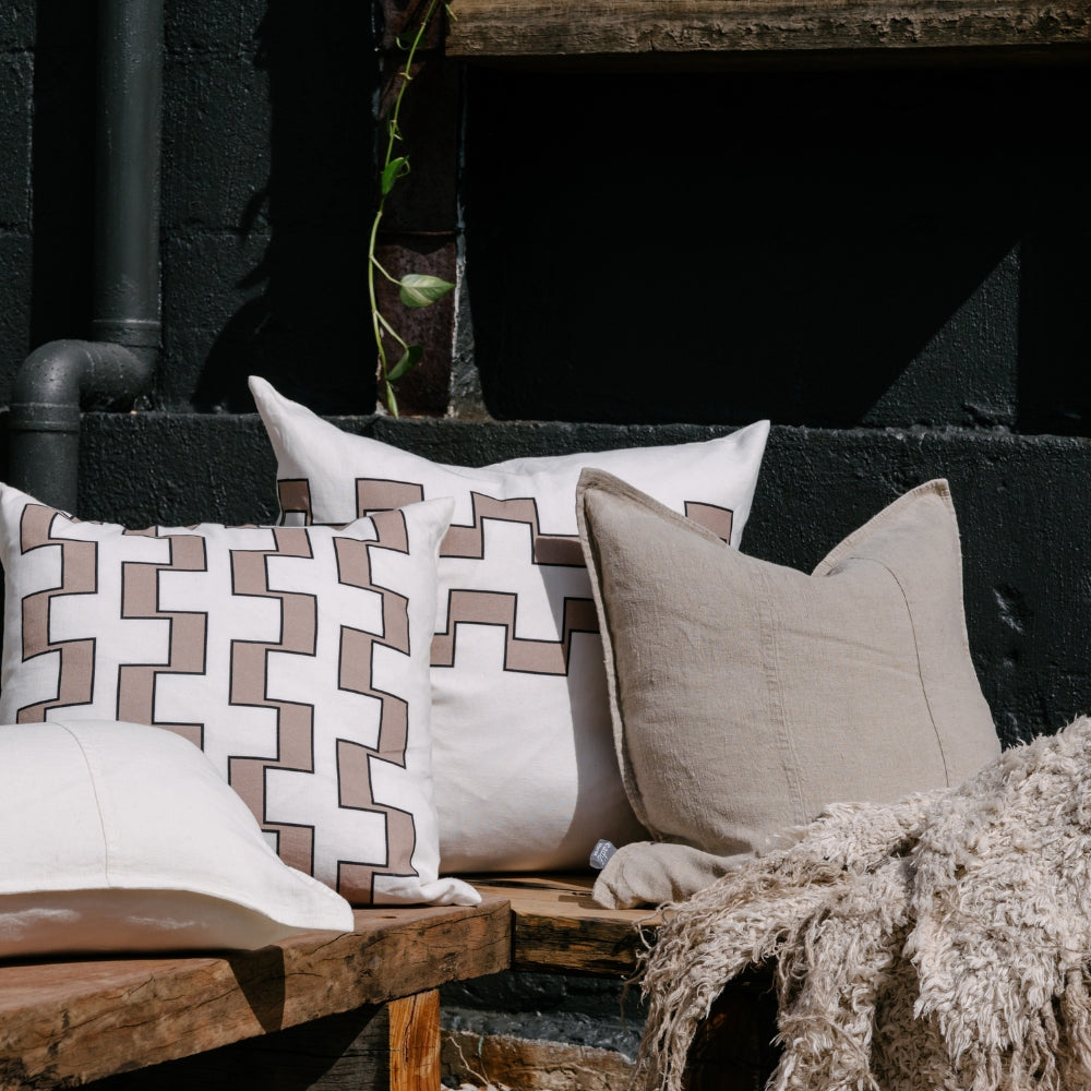 Decorative pillows on a wooden bench against a dark brick wall