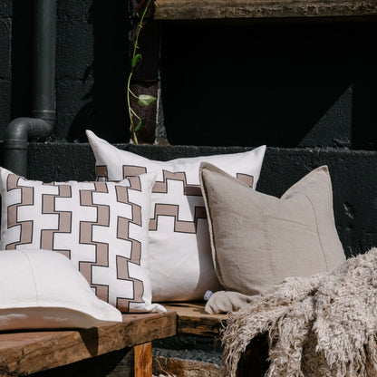 Decorative pillows on a wooden bench against a dark brick wall
