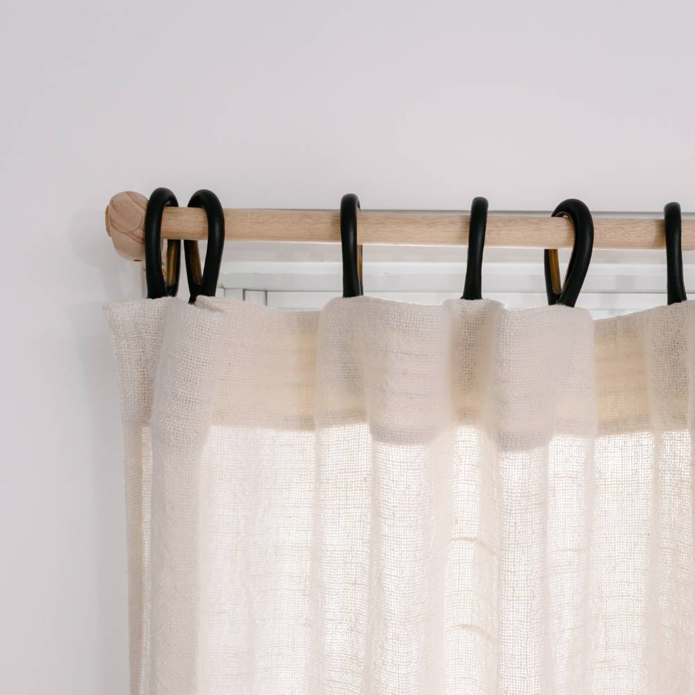 Sheer ivory curtain with black clip rings on a light wood rod.