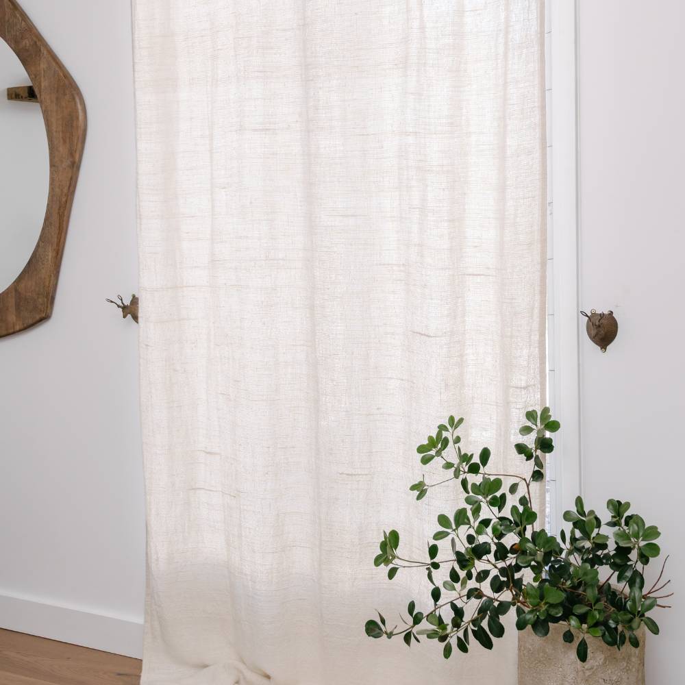 White textured curtain with a plant and wooden mirror on a white wall