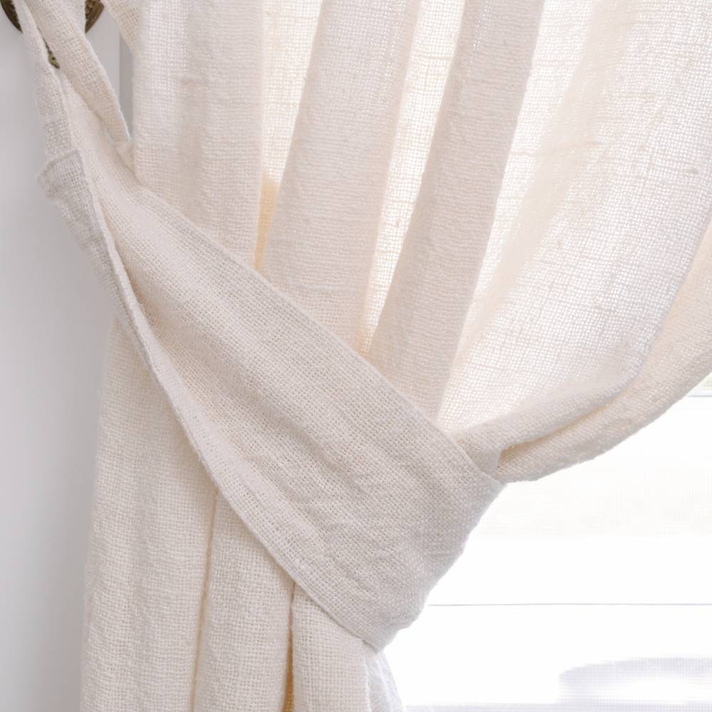 Close-up of a cream or off-white sheer curtain with a soft texture tied back with a fabric band on a white background