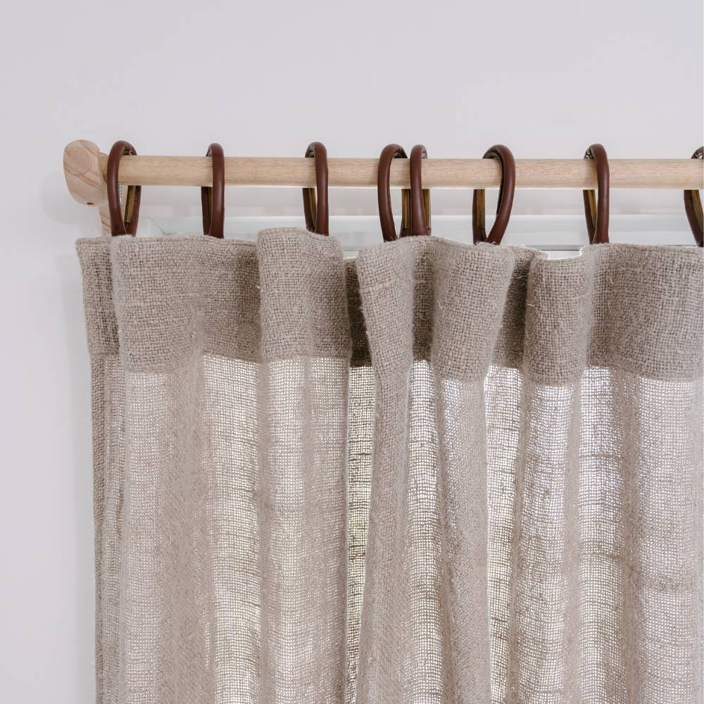 Textured natural or beige curtains hanging on a wooden rod against a white background