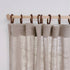 Textured beige curtains hanging on a wooden rod with brown leather rings against a white background