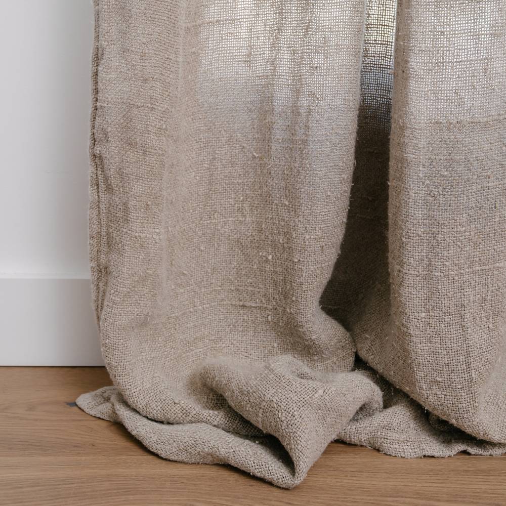 Close-up of textured beige curtain on a wooden floor with a white wall background