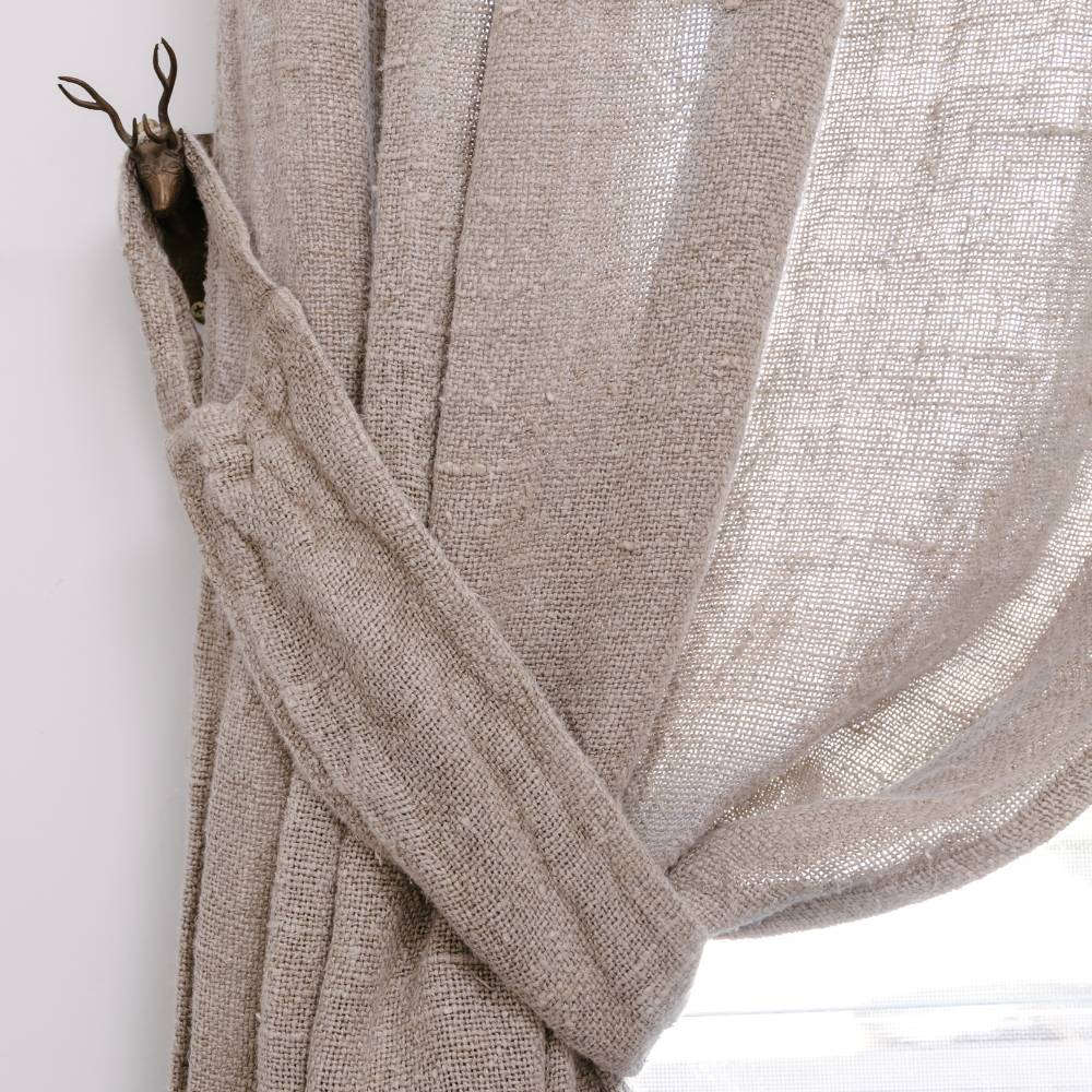 Beige curtain with a plant and wooden mirror on a white wall.