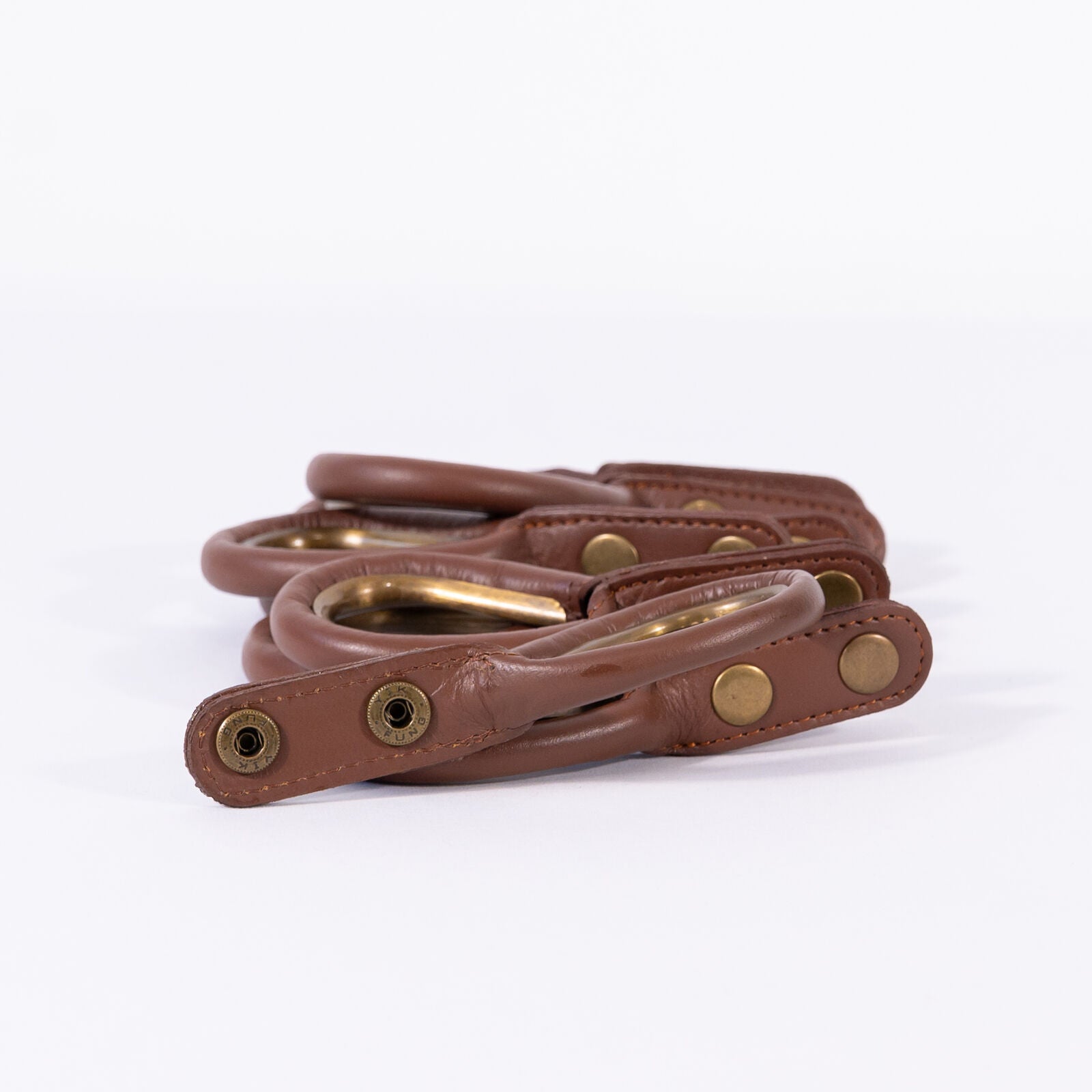 Set of brown leather rings with antique brass-colored rings and rivets on a white background