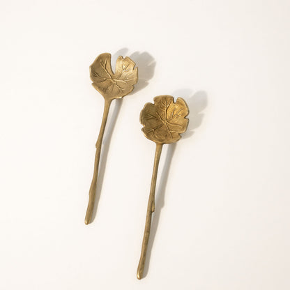 Set of gold-colored salad servers with a leaf design on a white background