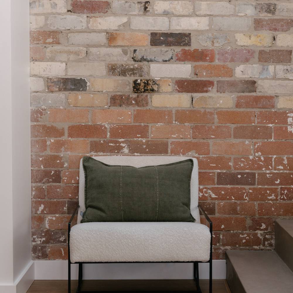 Olive green pillow on a white chair against a brick wall