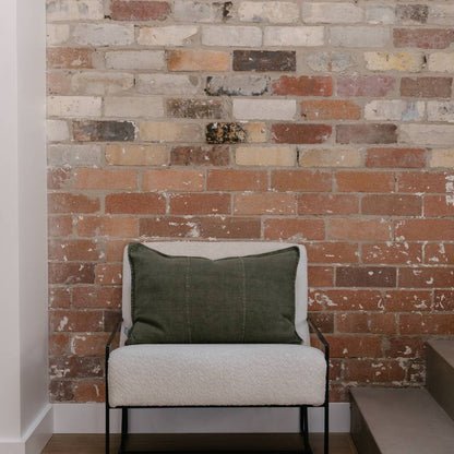 Olive green pillow on a white chair against a brick wall