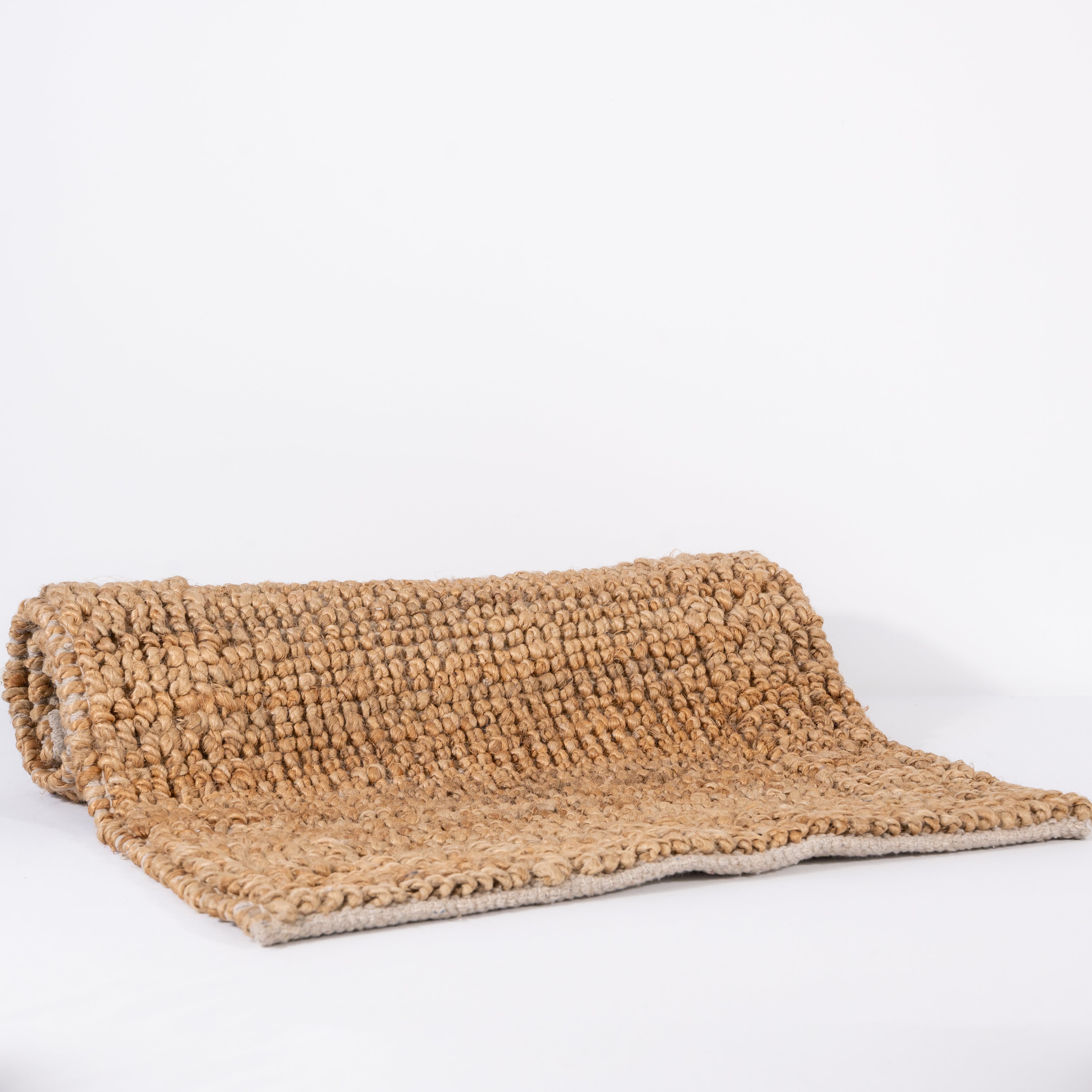 Natural handwoven jute rugs rolled and stacked on a white background