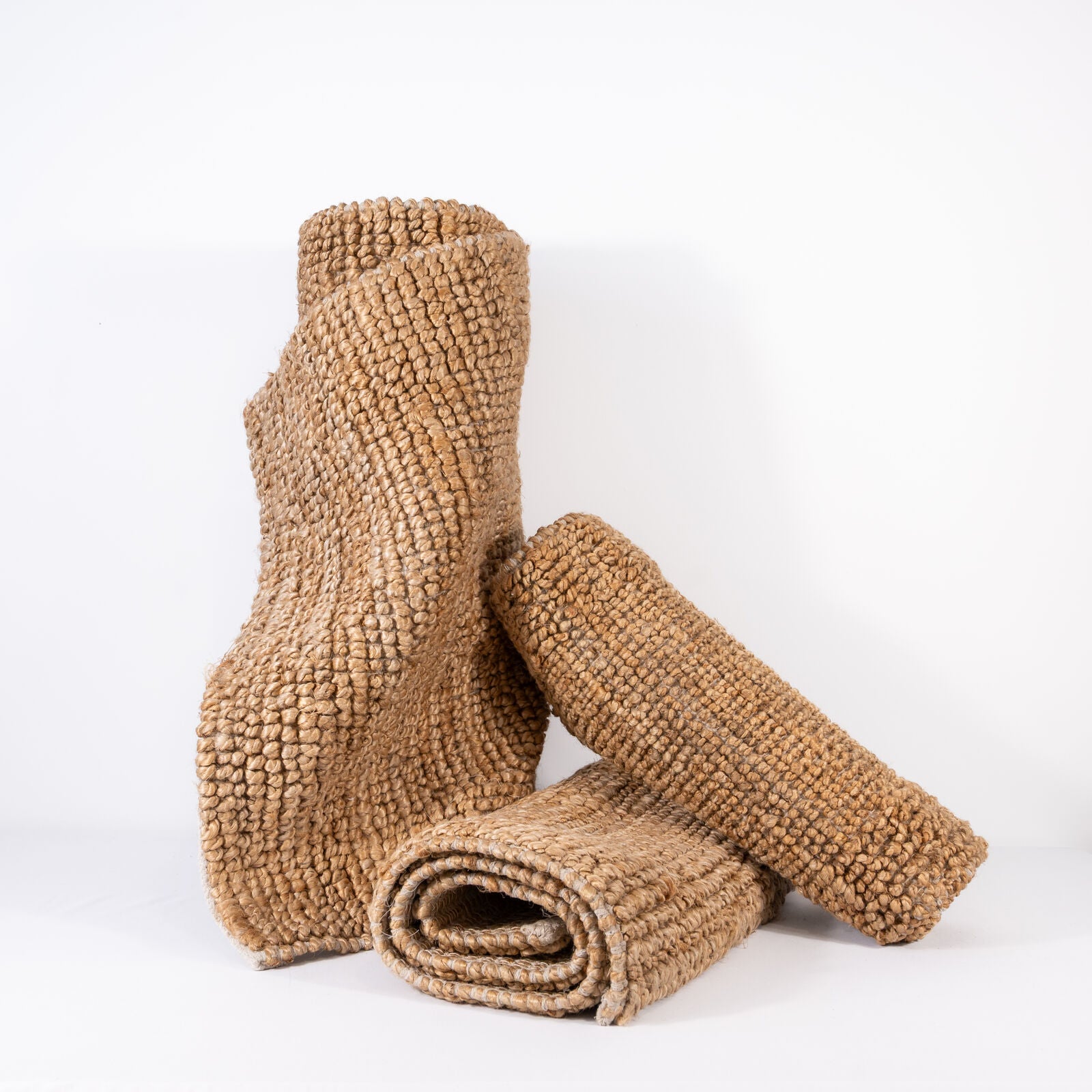 Natural handwoven jute rugs rolled and stacked on a white background
