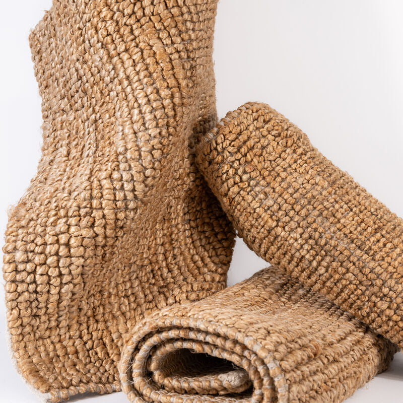Natural handwoven jute rugs rolled and stacked on a white background