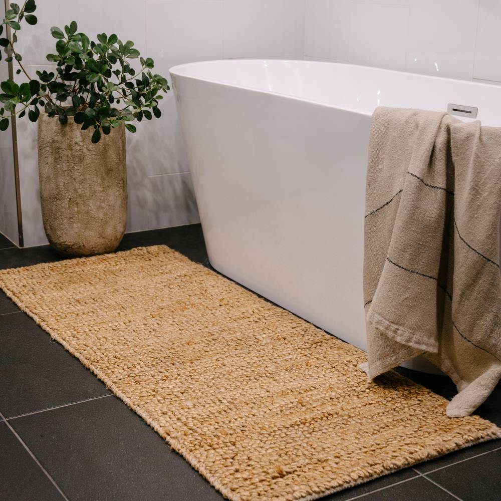 Bathroom with a woven bath mat, basket, and towel on a black tiled floor