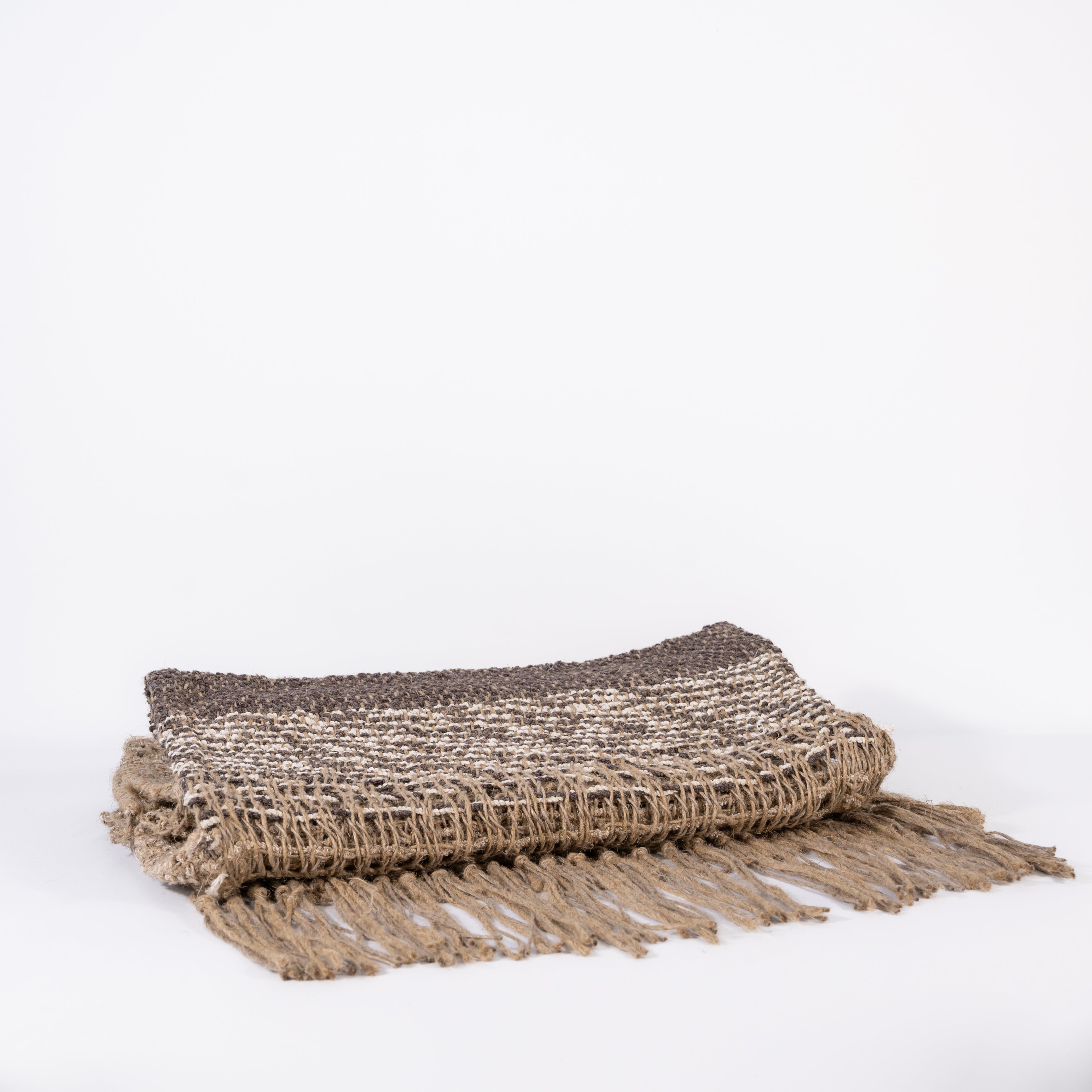 Folded handwoven natural jute rugs with fringe on a white background