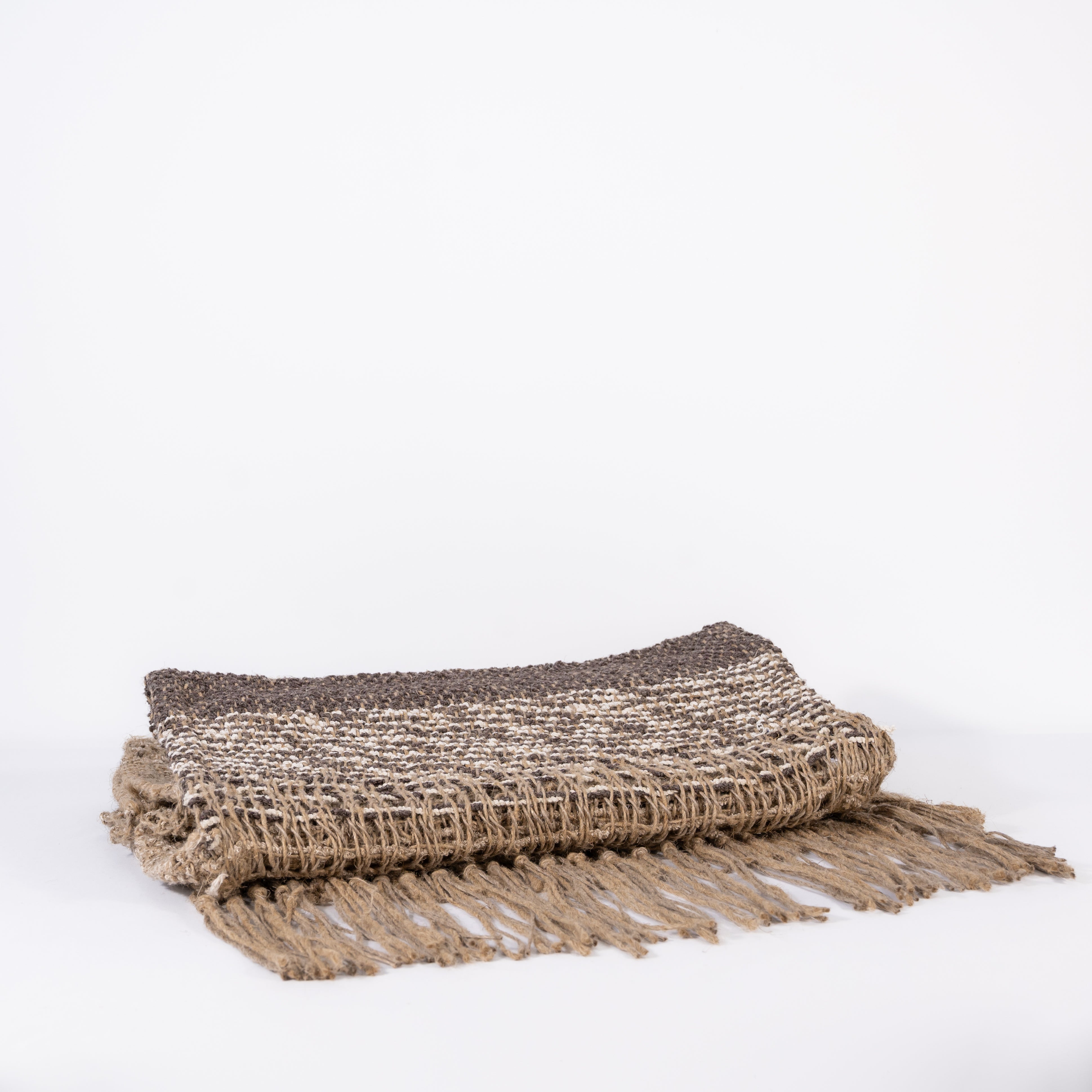Folded handwoven natural jute rugs with fringe on a white background