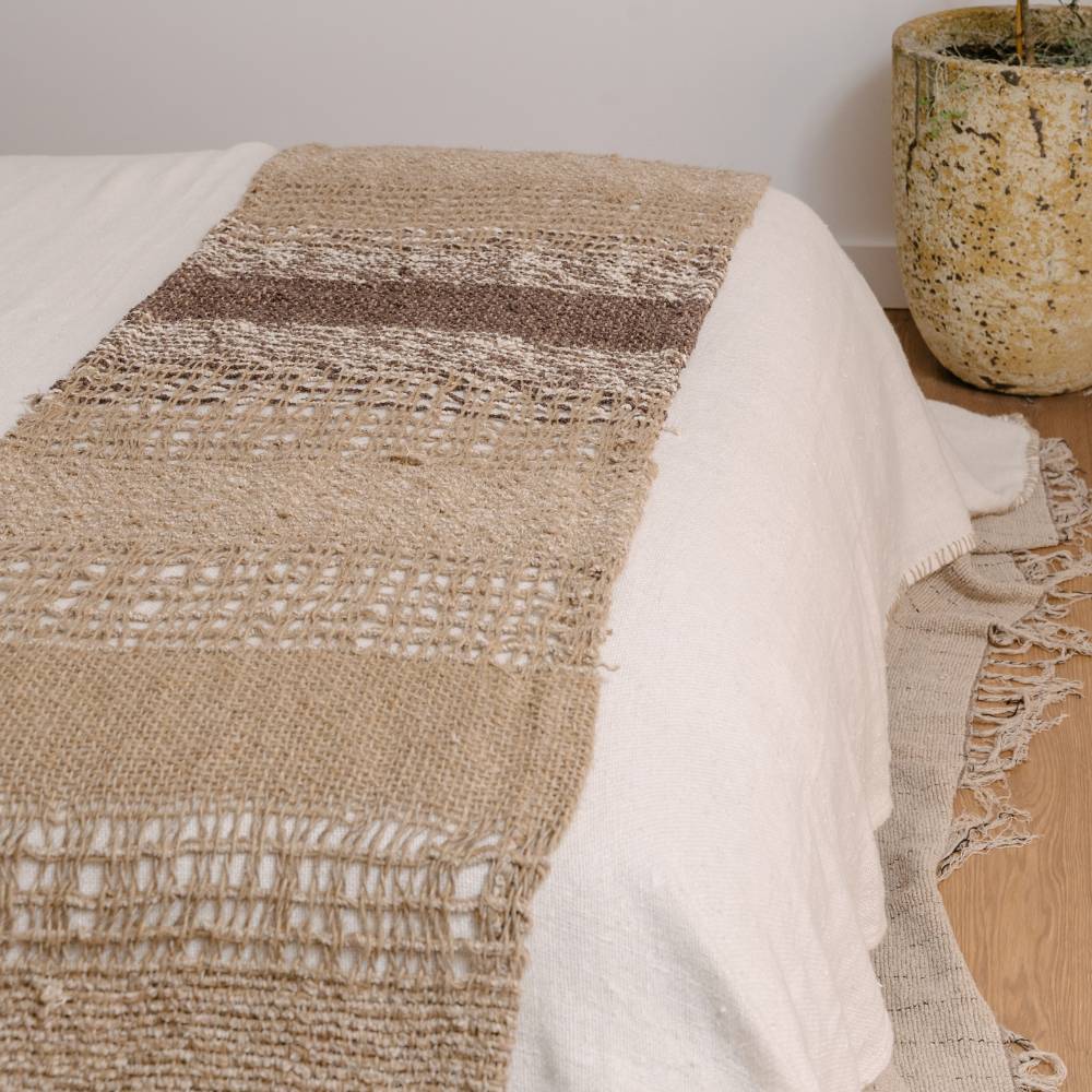 Textured blanket draped over a bed with a neutral color scheme, featuring a plant in the background.