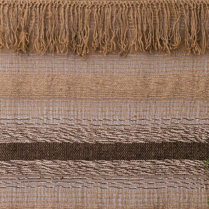 Textured blanket draped over a bed with a neutral color scheme, featuring a plant in the background.