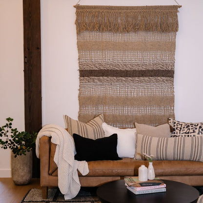 Textured blanket draped over a bed with a neutral color scheme, featuring a plant in the background.