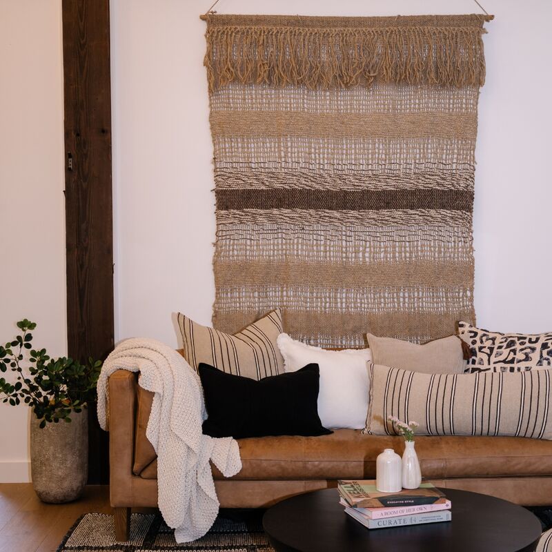 Textured blanket draped over a bed with a neutral color scheme, featuring a plant in the background.