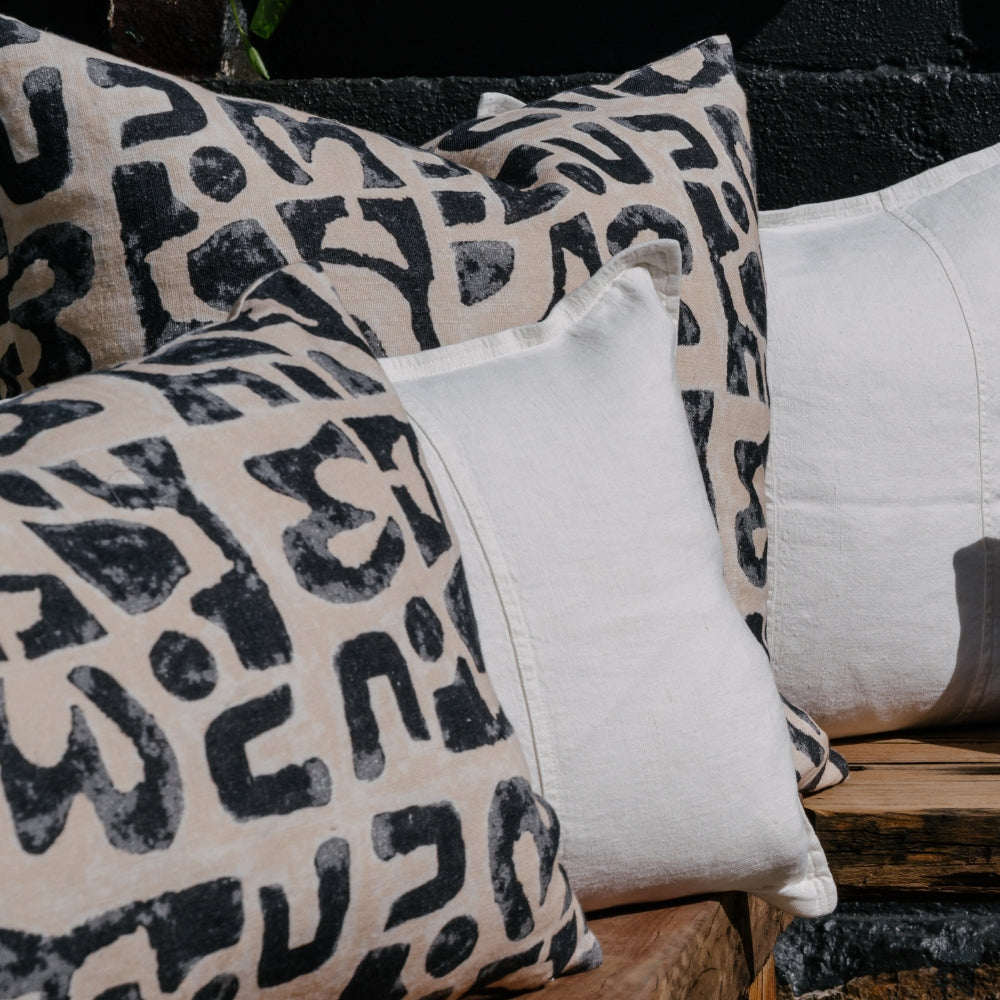 A close-up look at a collection of decorative pillows rests on a rustic wooden bench, against a dark, textured wall.