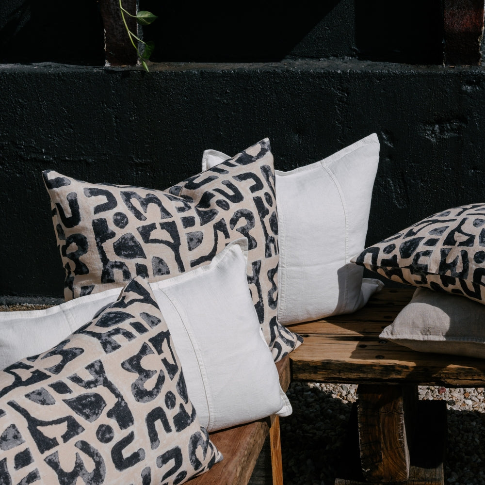 A collection of decorative pillows rests on a rustic wooden bench, against a dark, textured wall.
