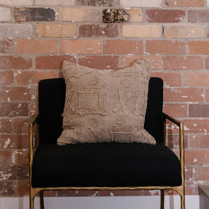 Textured beige pillow on a black chair against a brick wall