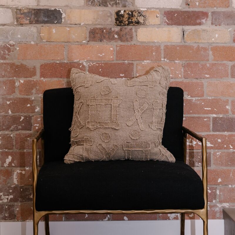Textured beige pillow on a black chair against a brick wall