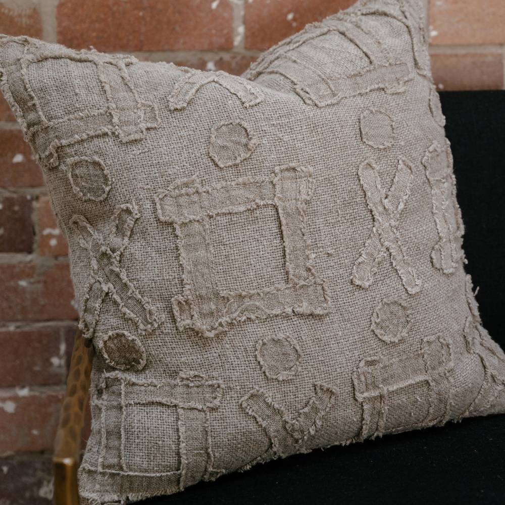 Textured beige pillow on a black chair against a brick wall