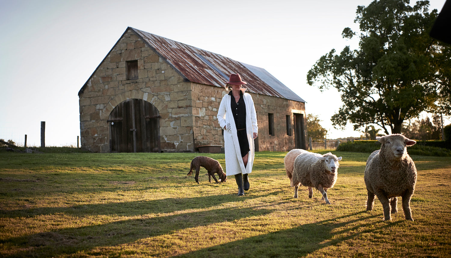 farm yard style backdrop with a boucle white coat and accent red brim hat and gum boots