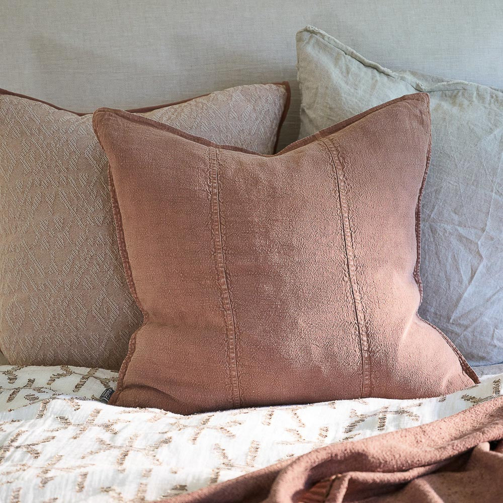 Three pillows with neutral colours on a bed