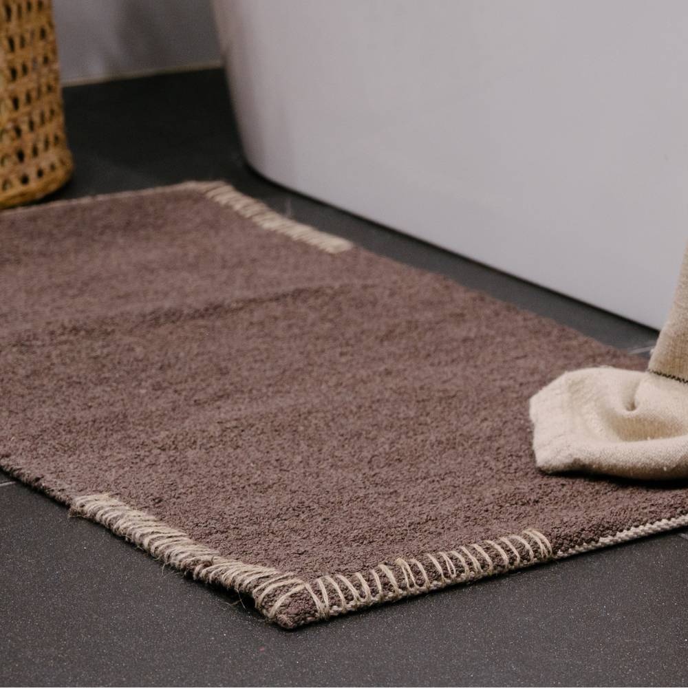 Dark brown bathmat and towel on a dark tiled bathroom floor with a white bathtub.