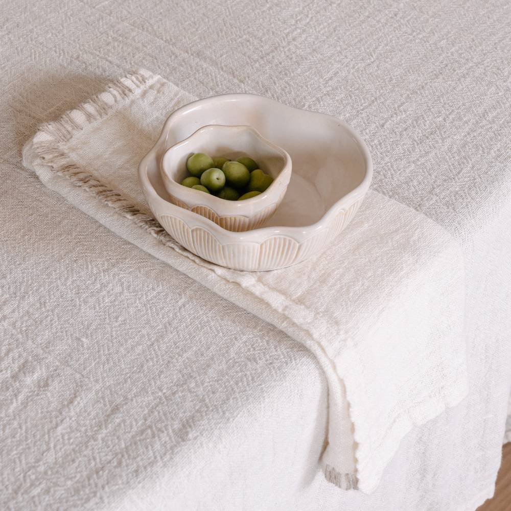White ceramic bowl with green olives on a textured white surface