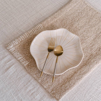 White ceramic plate with gold fork and spoon on a textured beige placemat.