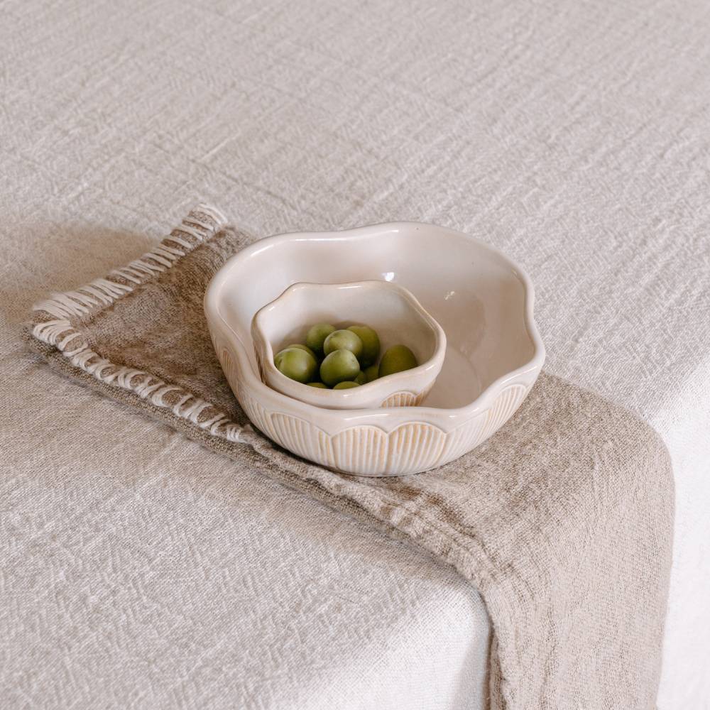 A textured beige linen table napkin with a decorative stitched edge is draped over a light tablecloth, holding two bowls.