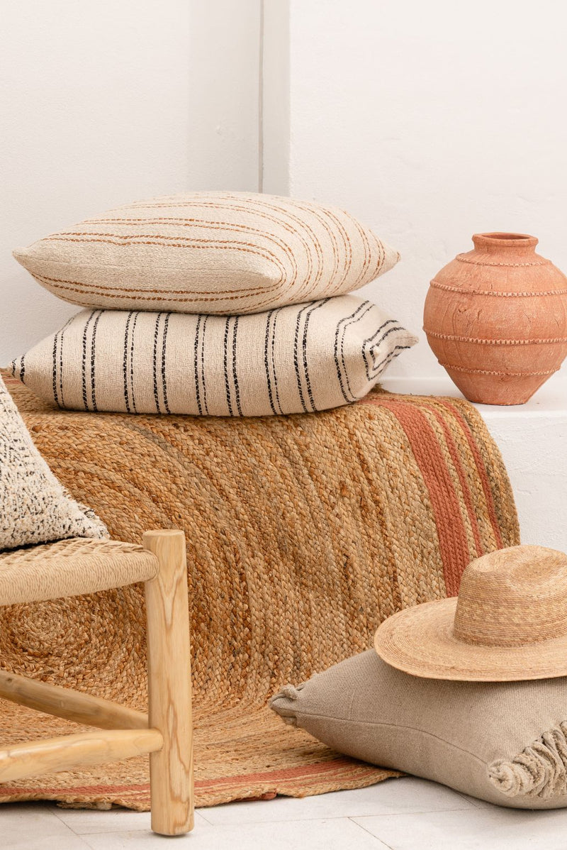 Woven chair with textured linen Eadie cushions and a hat, set against a white wall. Summer mediterranean feel.