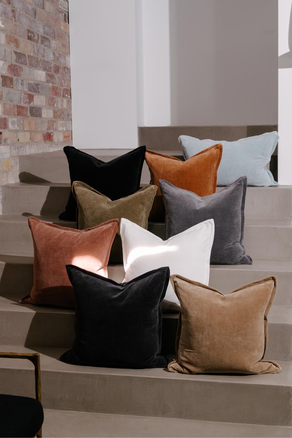 Collection of colorful velvet cushions by Eadie Lifestyle on a staircase with a neutral background