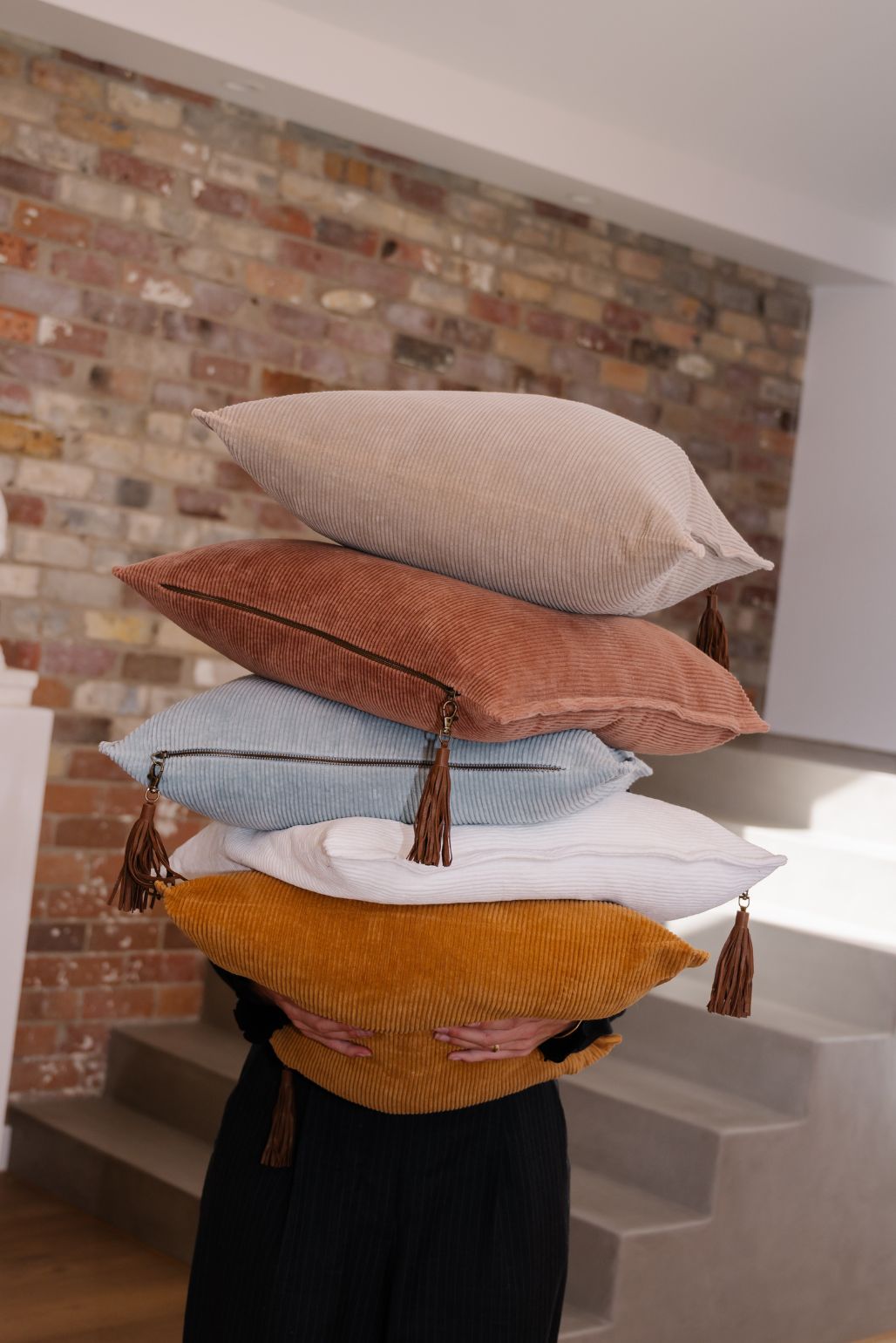 Stack of colorful Eadie cord cushions held by a person against a brick wall.
