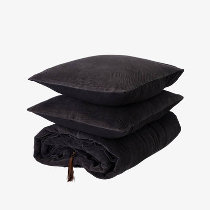Stack of black textured pillows and a blanket on a white background