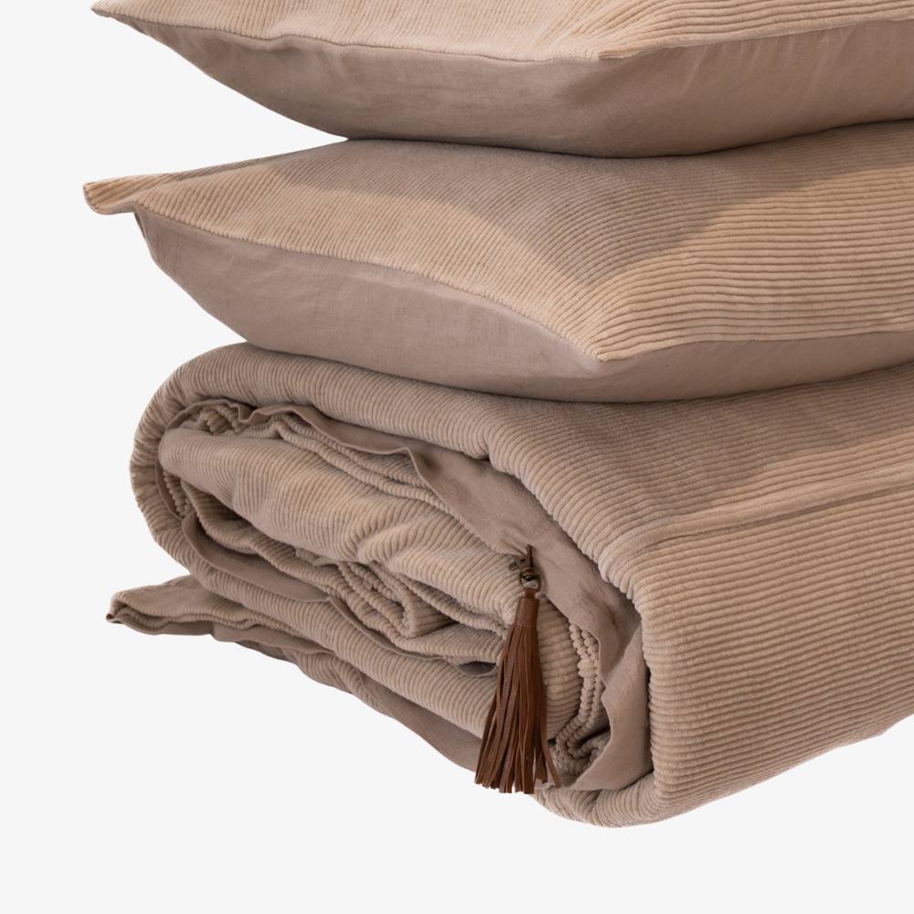 Stack of beige textured pillows and blanket with tassel on a white background