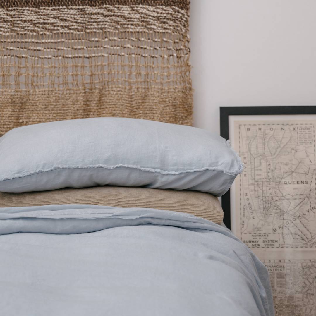 Bed with light blue bedding and pillows against a textured wall and map decor.