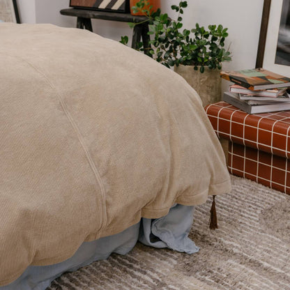 Beige comforter on a bed with a plant and books in the background