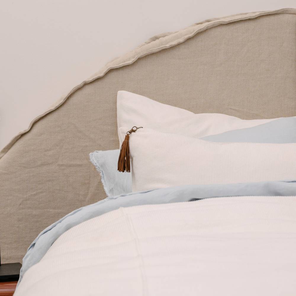 Neatly made bed with light blue bedding and a decorative pillow featuring a tassel.