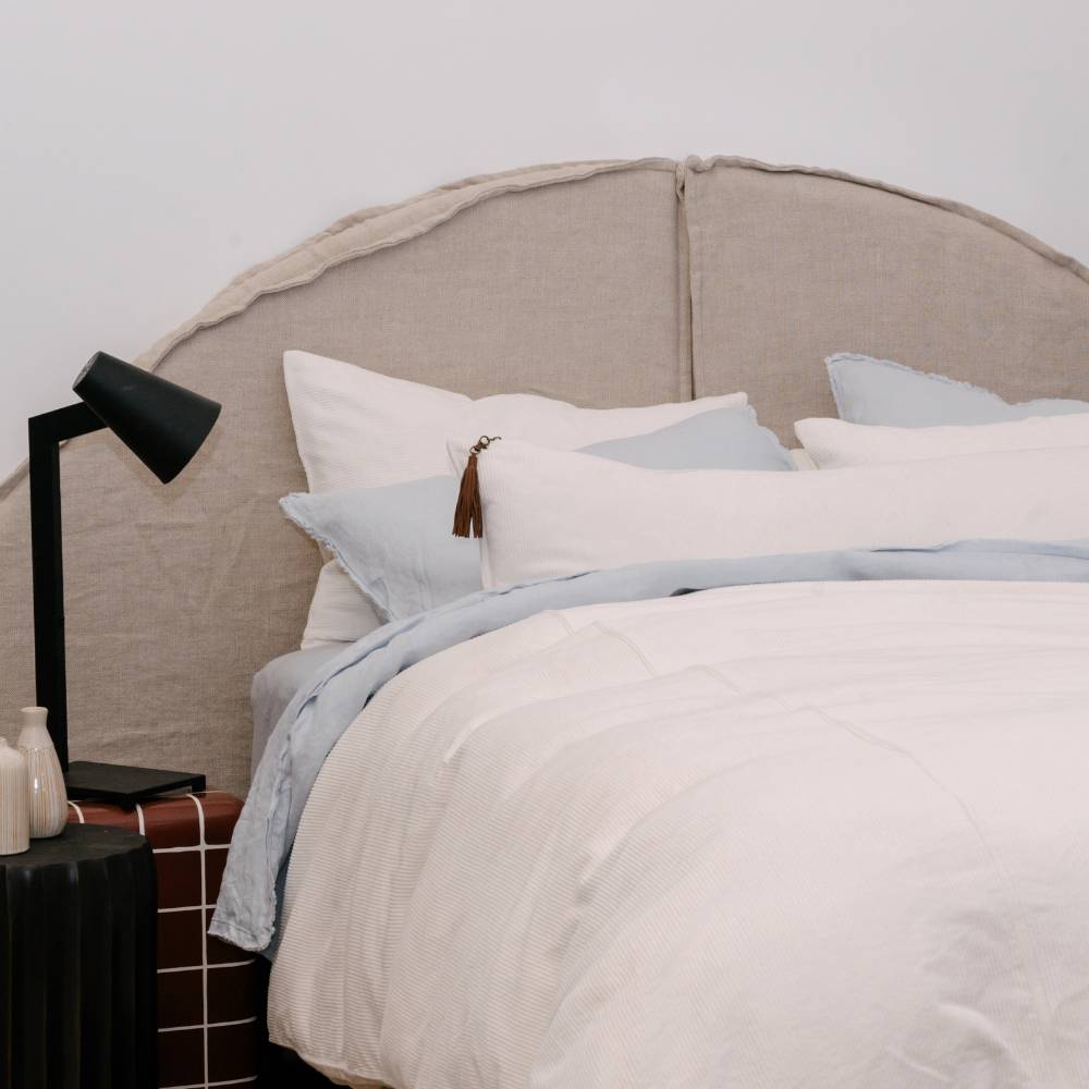Neatly made bed with light-colored bedding and pillows, featuring a lamp on a nightstand.