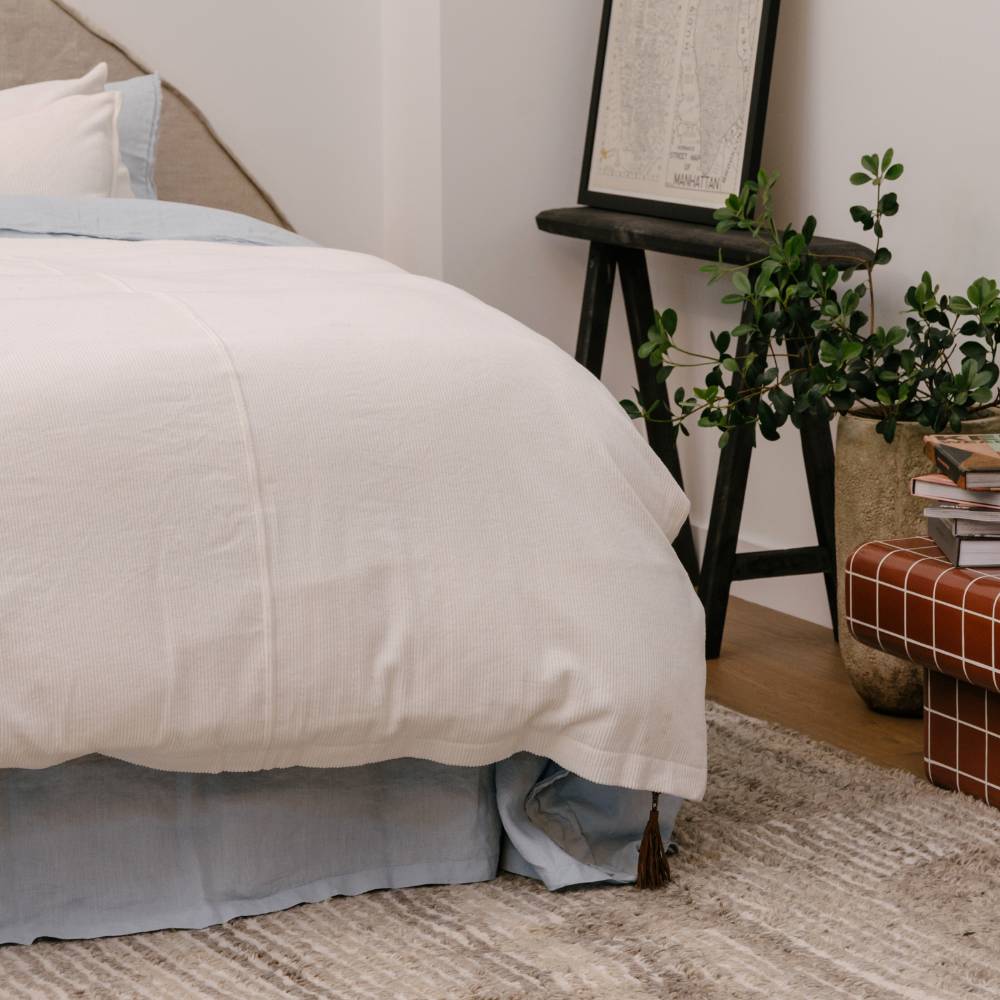 Neatly made bed with white bedding and gray skirt in a bedroom setting.