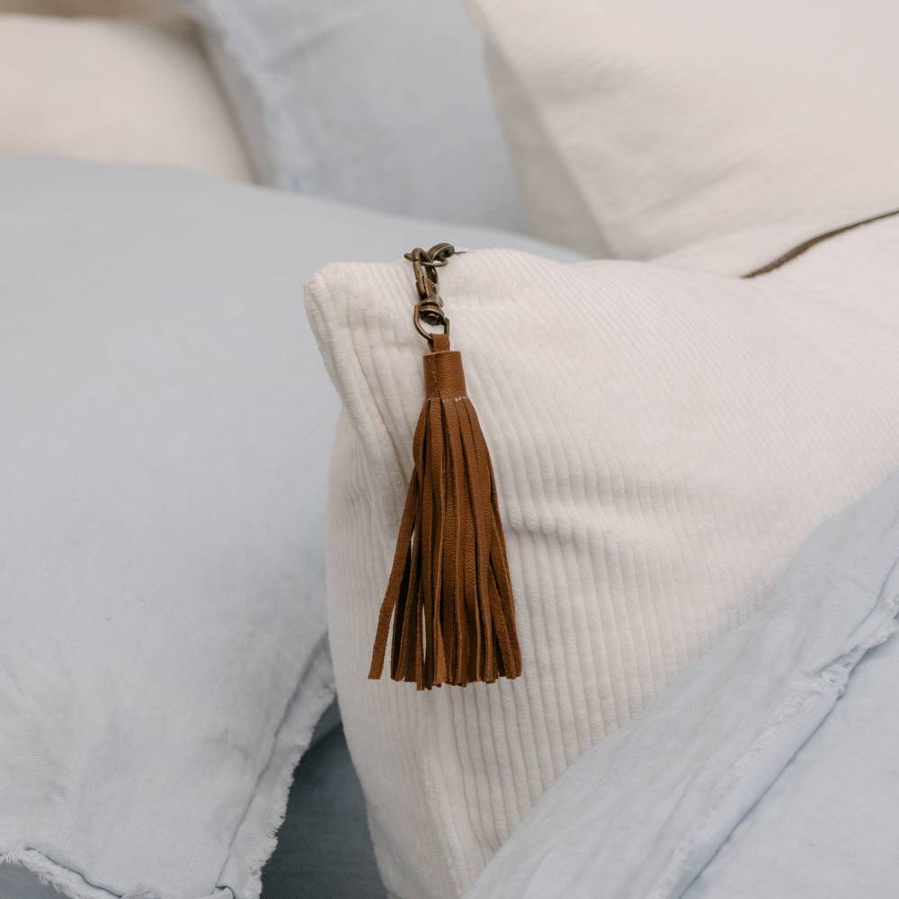 Brown leather tassel keychain on a textured pillow with soft pastel colors.